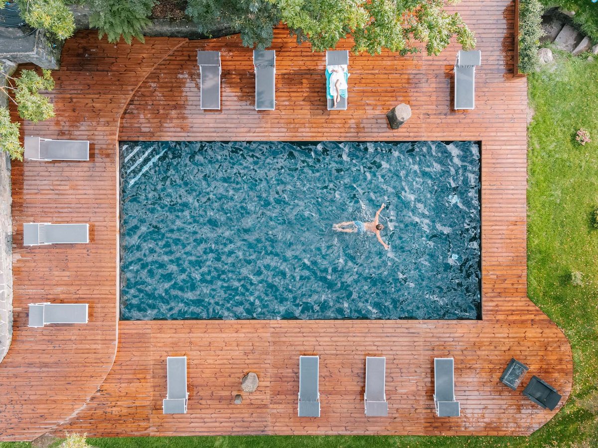 Vogelperspektive auf Außenpool mit Liegestühlen und schwimmender Person Außenpool mit schwimmender Person und Liegestühlen